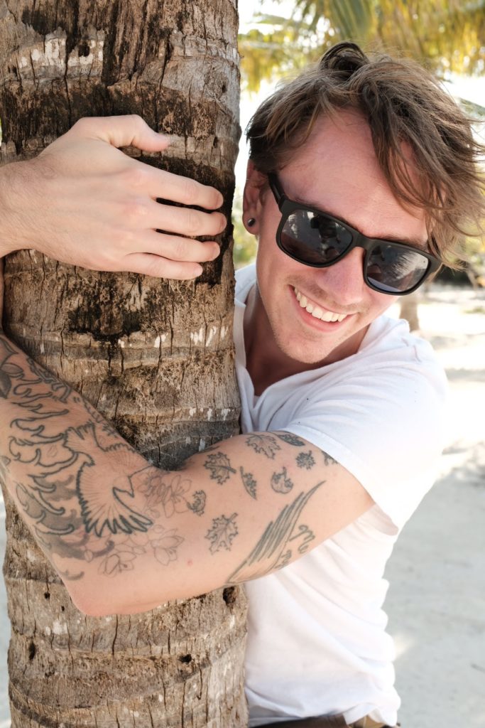 Dan in sunglasses hugging a palm tree